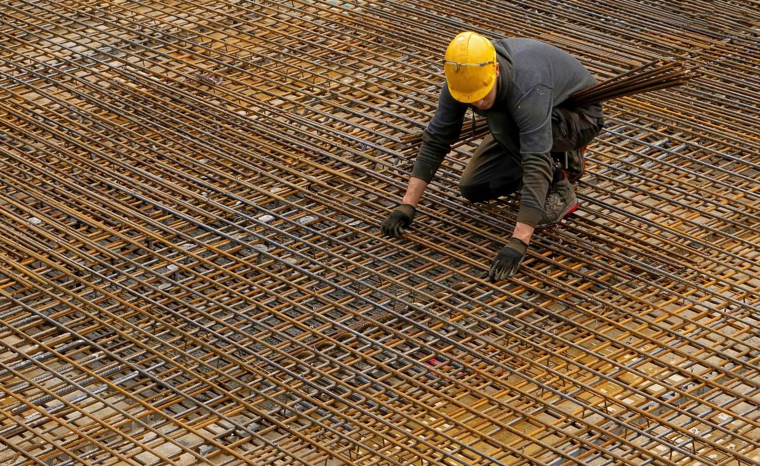 A worker in a yellow hard hat laying rebar across a slab